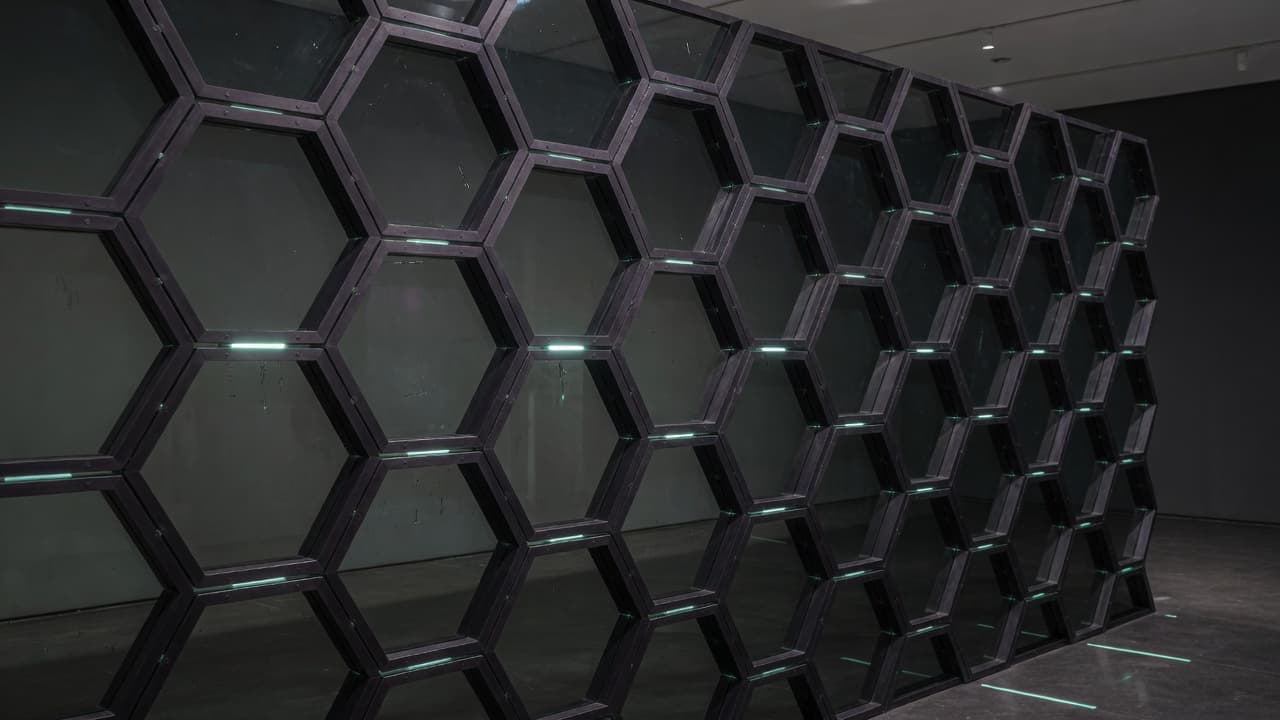 Dark anodized honeycomb lattice with sparse teal status light.